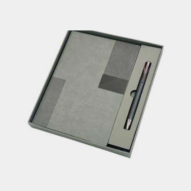 Two-tone grey PU notebook with metal logo plate and matching pen in a grey tray
