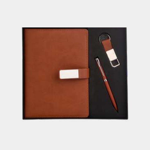 Tan notebook with metal pen and leather keychain set into a contrasting black tray