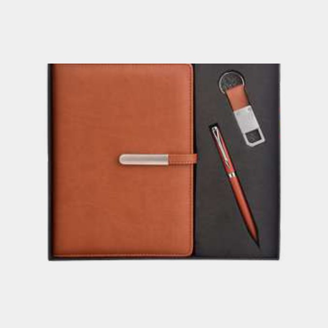 Tan leather notebook with metal keychain and red-barrel pen in a two-tone tray